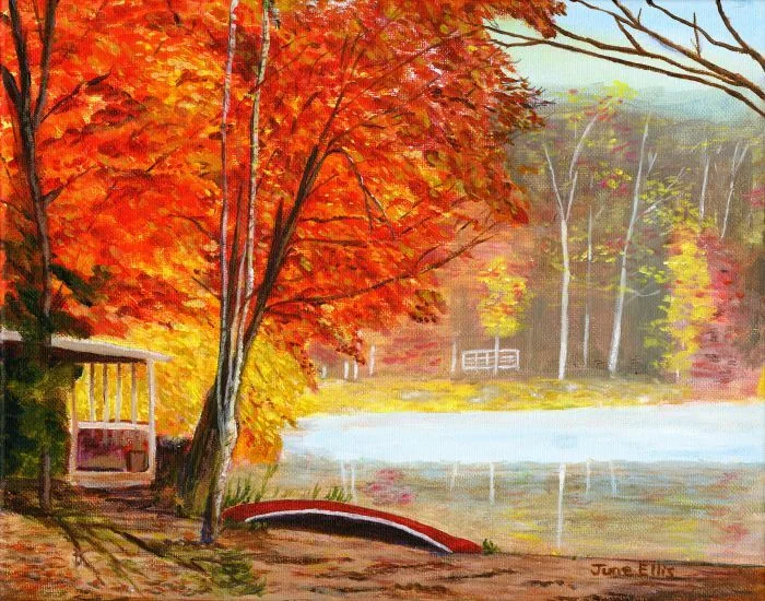 Glowing red, orange and yellow leaves on a tree overlooking the lake. A canoe under the tree